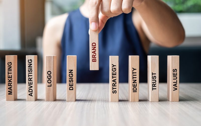 Businesswoman hand placing or pulling wooden Dominoes with BRAND text. and Marketing, Advertising, Logo, Design, Strategy, Identity, Trust and Values. Product development concept